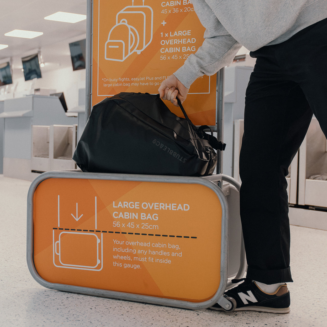 a man placing an All Black kit Bag 30L backpack into the hand luaggage size checker at an airport