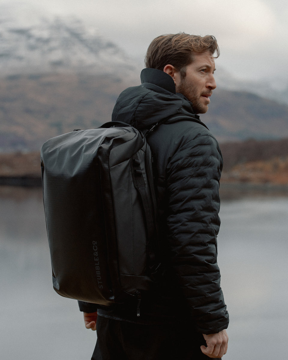 a man standing in front of a lake in Scotland wearing a kit bag 30l on his back