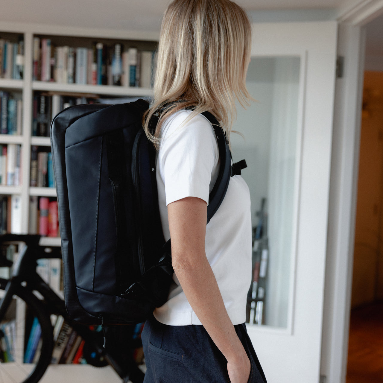A woman facing side on wearing a Kit Bag 30L in Midnight Blue on her back