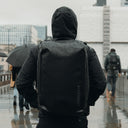 A man facing away in the rain wearing an All Black Kit Bag 30L on his back