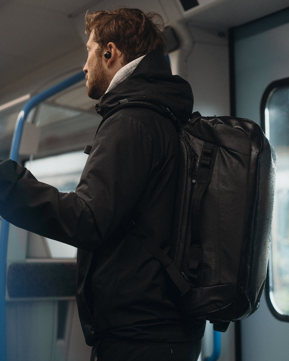 a man standing on a train wearing a black kit bag 30l on his back 