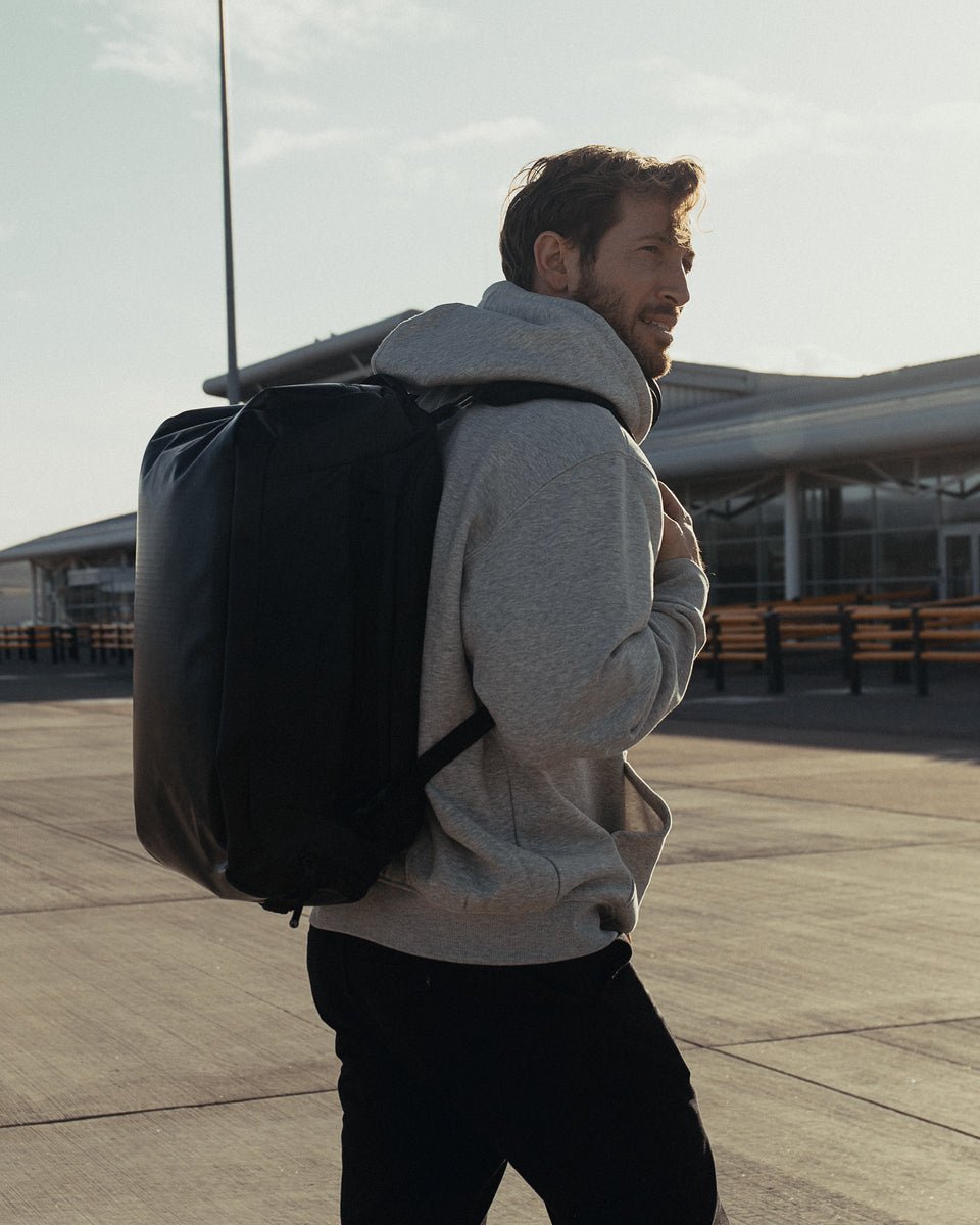 a man walking outside an airport wearing an kit bag 30l on his back