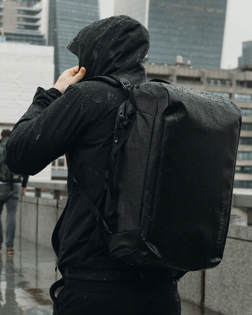 A man wearing a black Kit Bag 30L on his back in the rain