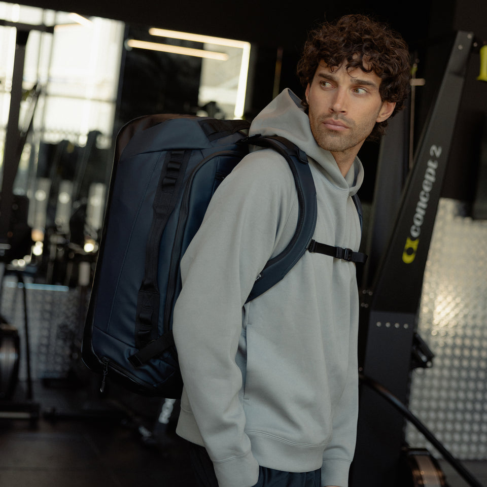 A man standing side on in a gym wearing a Kit Bag 40L in Midnight Blue