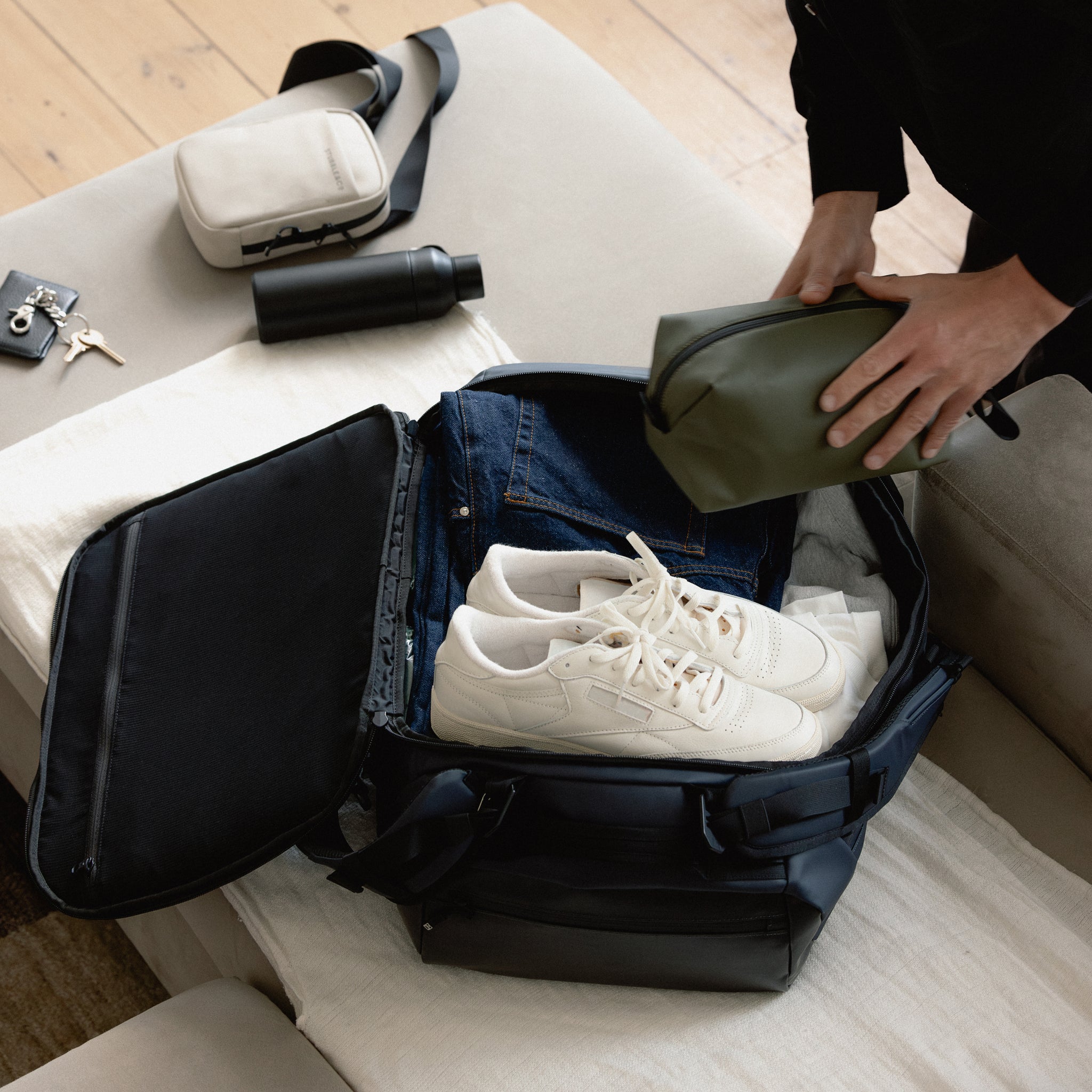 A man packing a Kit Bag 40L in Midnight Blue as he puts a Stubble & Co green wash bag inside