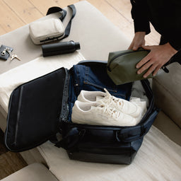 A man packing a Kit Bag 40L in Midnight Blue as he puts a Stubble & Co green wash bag inside