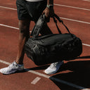 A man walking holding the Kit bag 40L in All Black by his side like a Duffel Bag