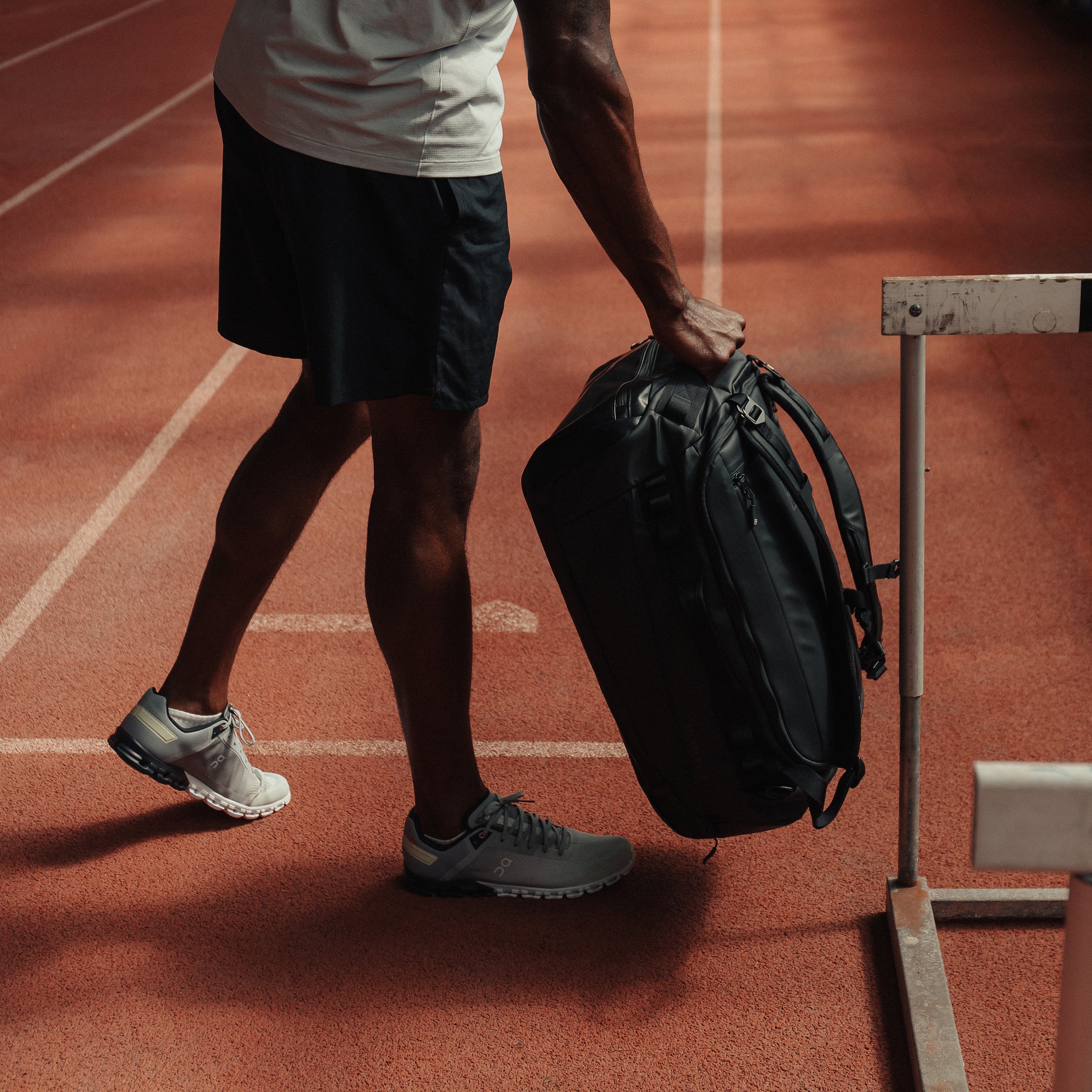 A man placing down an All Black Kit Bag 40L down on the floor of an athletics track