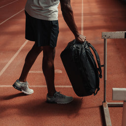 A man placing down an All Black Kit Bag 40L down on the floor of an athletics track