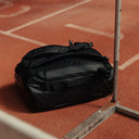 A Kit Bag 40L in All Black on the floor of an indoor running track