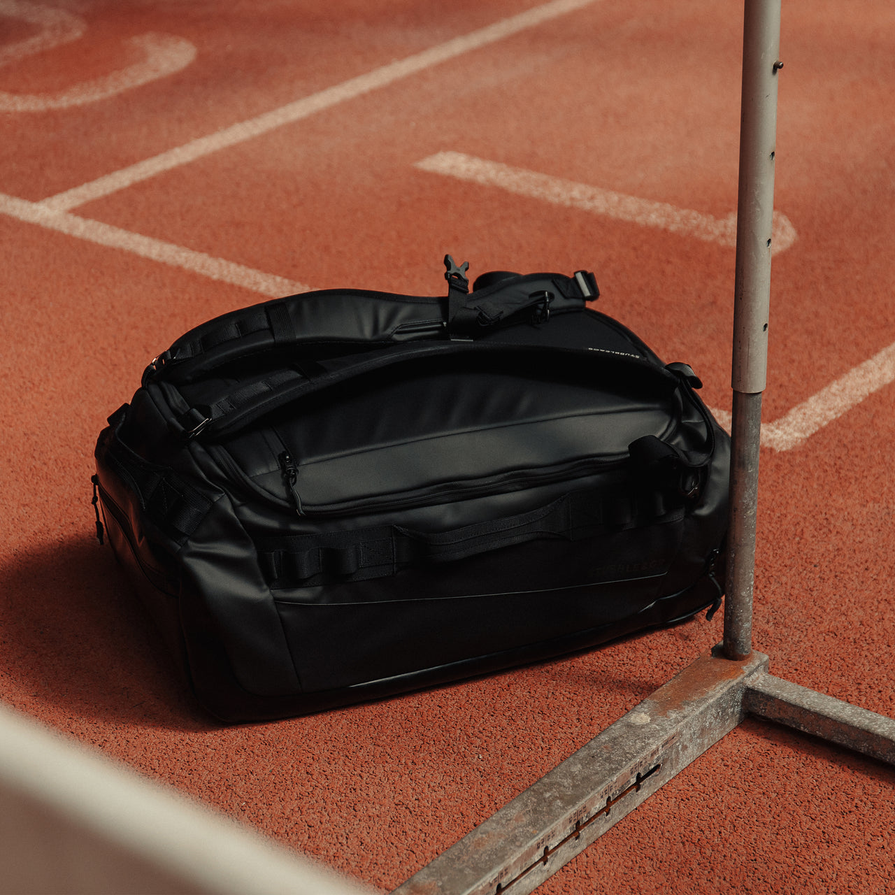 A Kit Bag 40L in All Black on the floor of an indoor running track