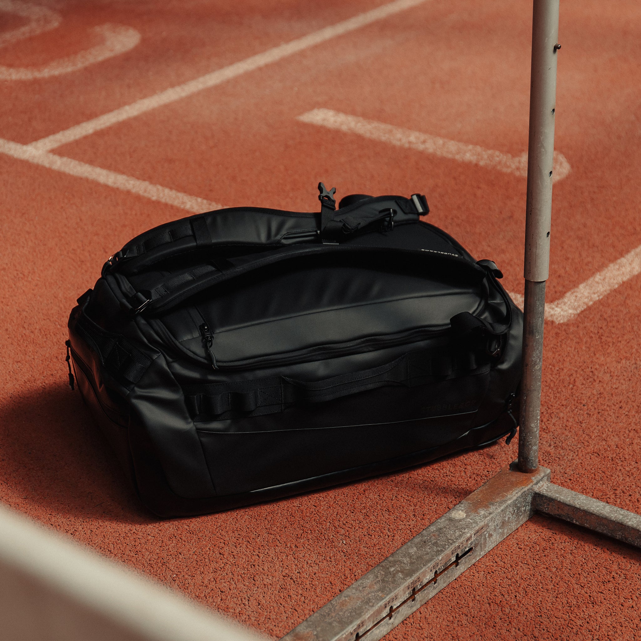 A Kit Bag 40L in All Black on the floor of an indoor running track