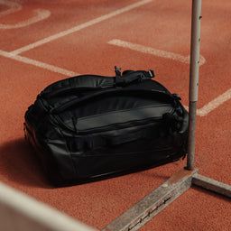 A Kit Bag 40L in All Black on the floor of an indoor running track