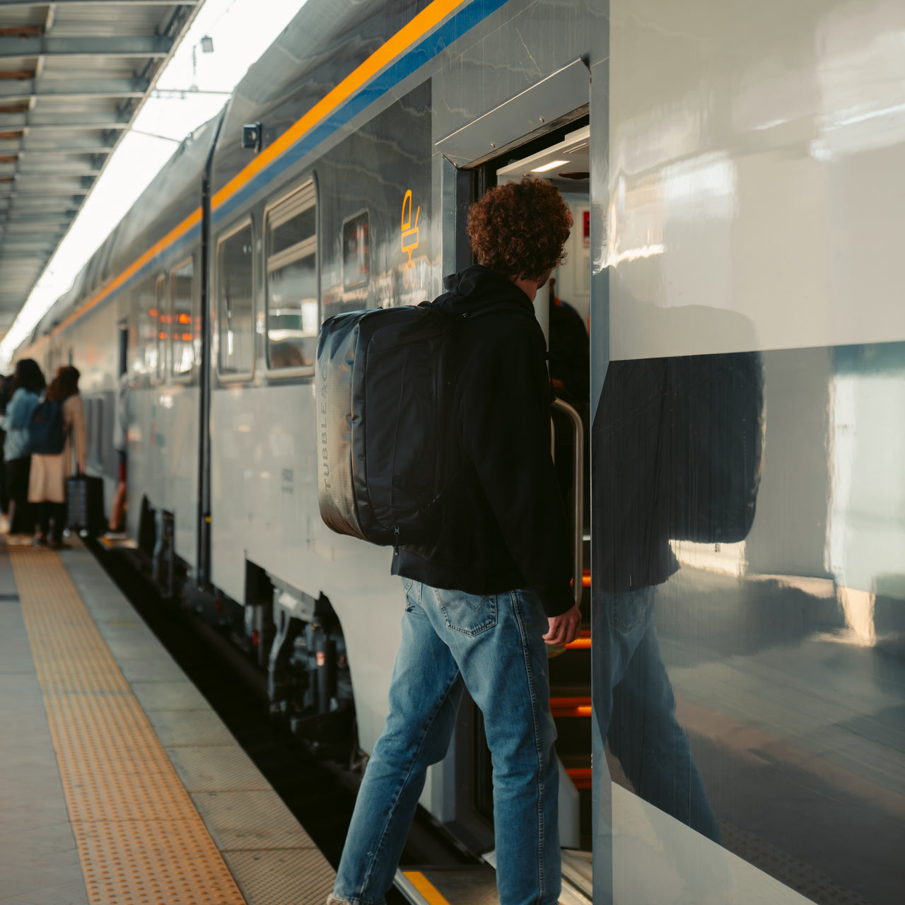 A man wearing an All Black Kit Bag 40l on his back as he boards a train