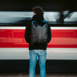 A man wearing an All Black Kit Bag 40L in front of a train