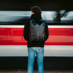 Person on a platform as a train passes, wearing the Kit Bag 40L in All Black