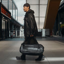 A man walking into airport holding an All Black Kit Bag 65L by his side