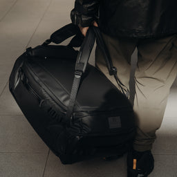 A close up of a man carrying an All Black Kit Bag 65L by his side.