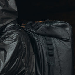 a close up shot of an All Black Kit Bag 65L in the rain on a mans back