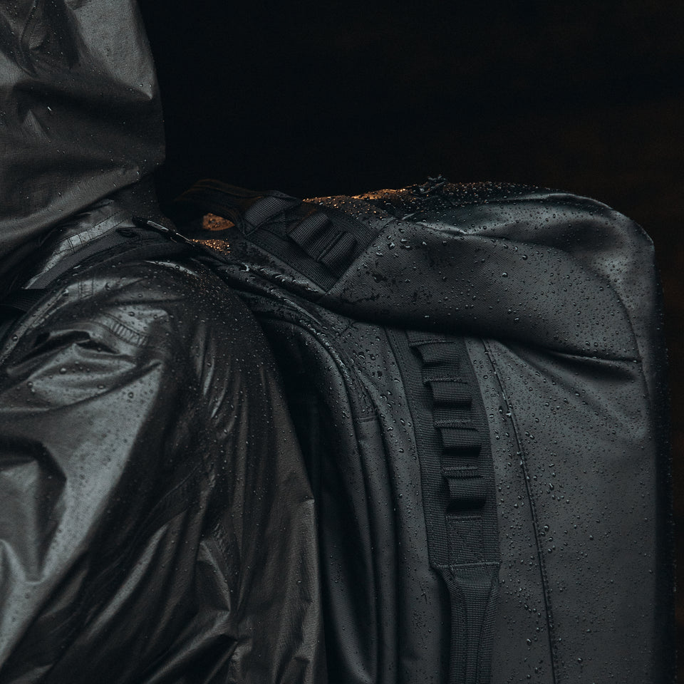 a close up shot of an All Black Kit Bag 65L in the rain on a mans back