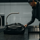 A man collecting an All Black Kit bag 65L off the baggage carousel at an airport