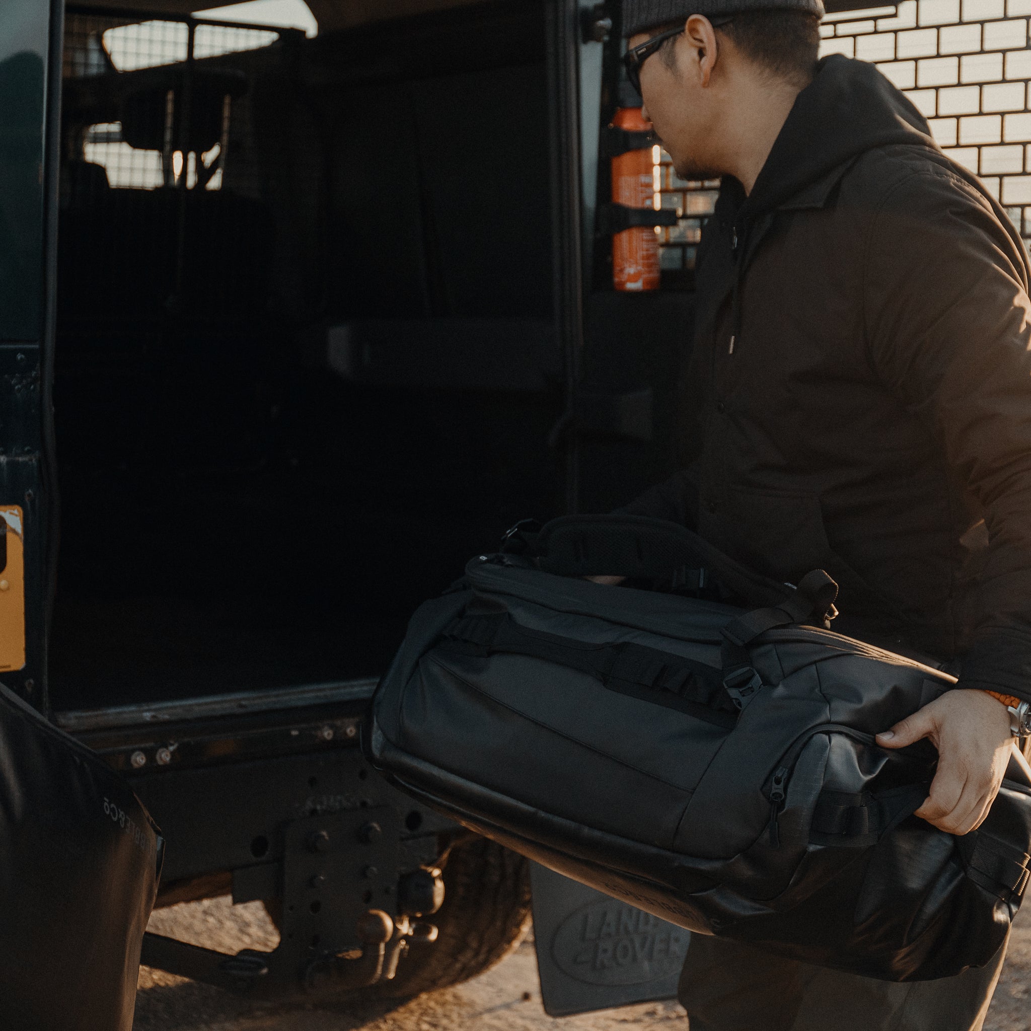 a man putting an All Black Kit Bag 65L into the boot of his car