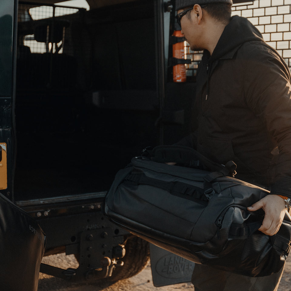 a man putting an All Black Kit Bag 65L into the boot of his car
