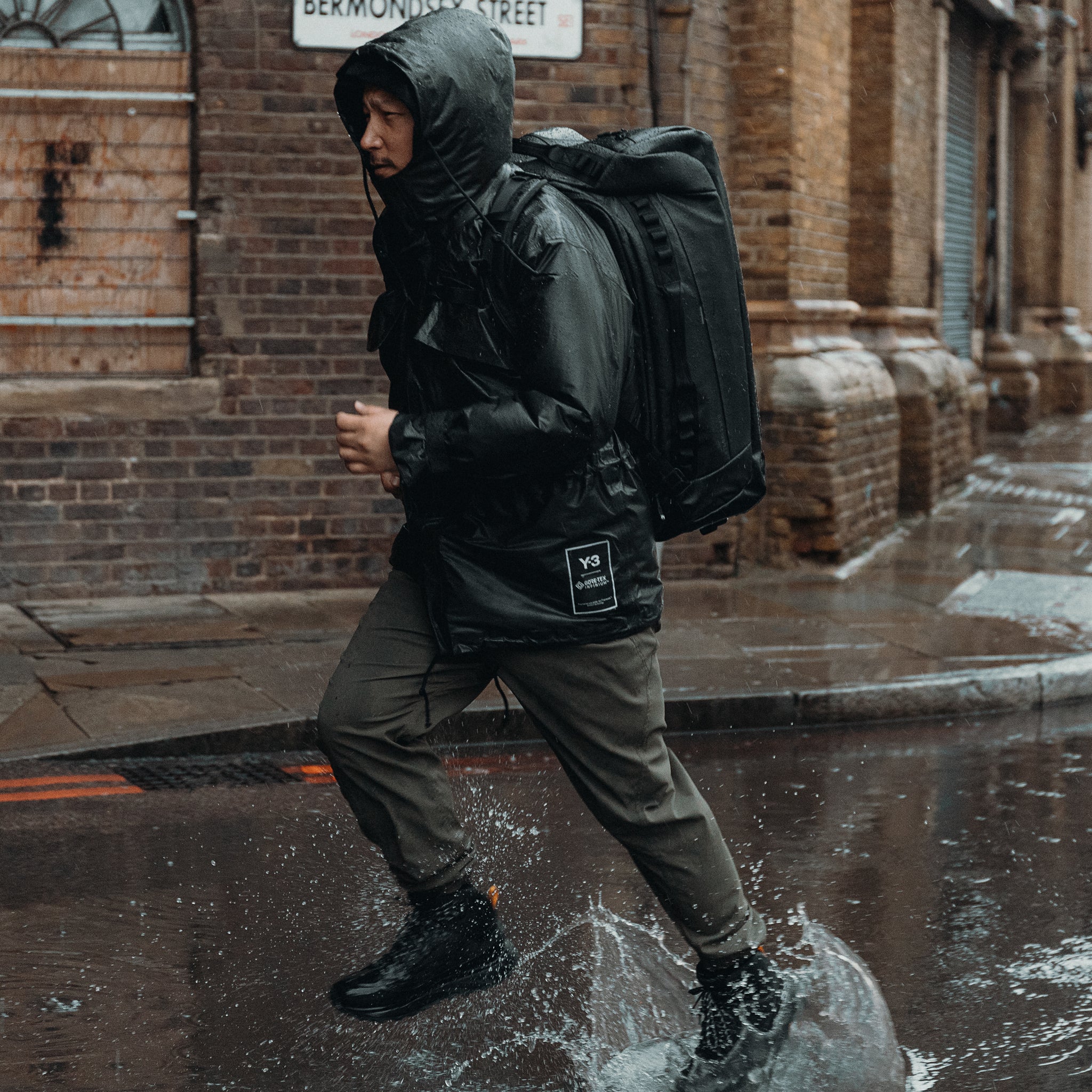 A man running through a puddle in the rain with an All Black Kit Bag 65L on his back