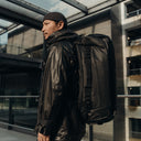 A man wearing an All Black Kit Bag 65L on his back