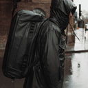 A man wearing an All Black Kit Bag 65L on his back in the rain