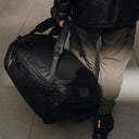 A close up of a man carrying an All Black Kit Bag 65L by his side.
