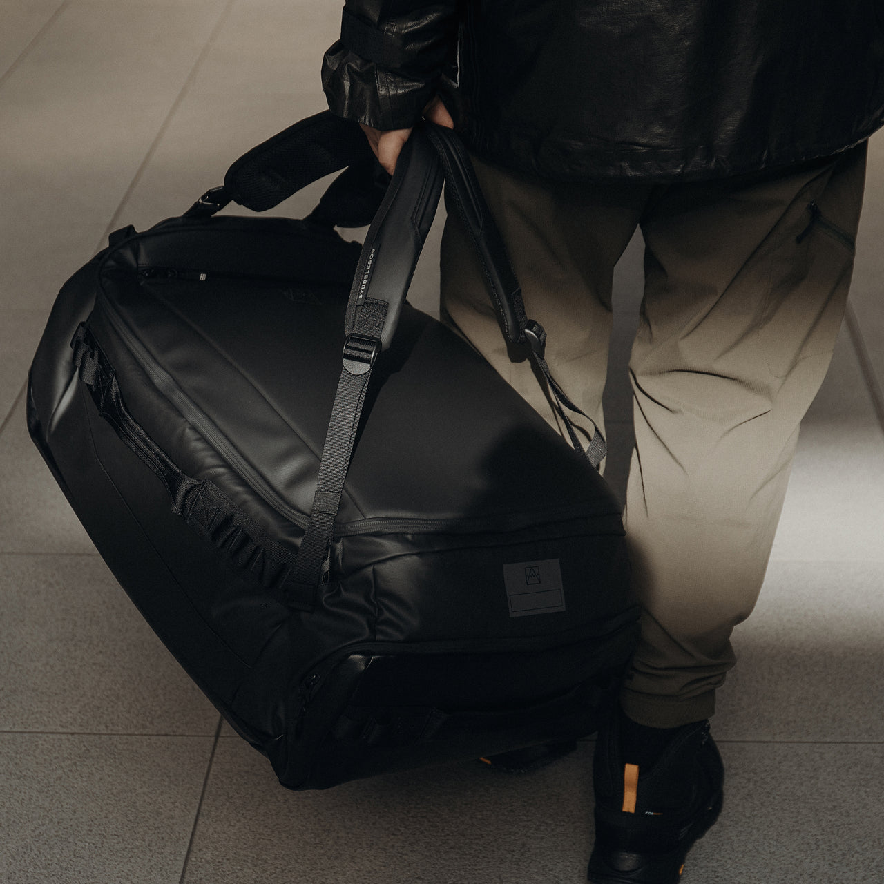 A close up of a man carrying an All Black Kit Bag 65L by his side.