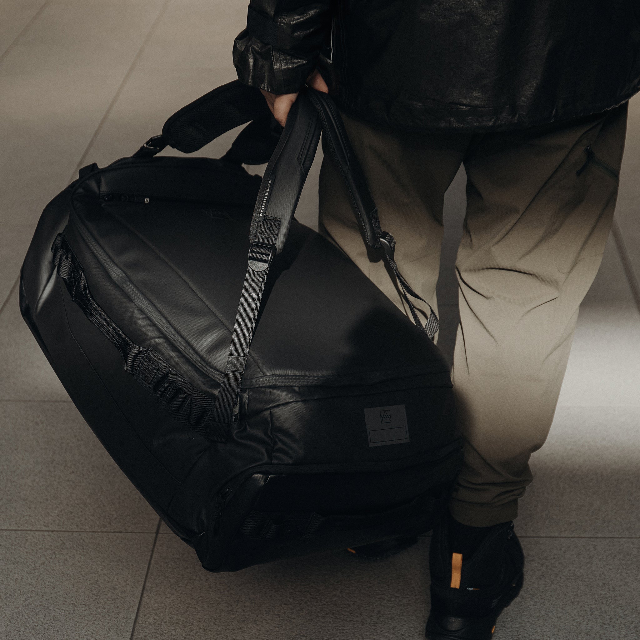 A close up of a man carrying an All Black Kit Bag 65L by his side.