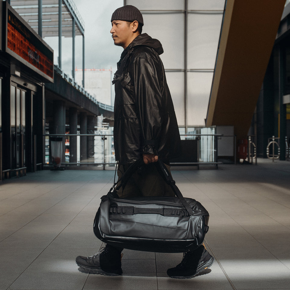 A man walking into airport holding an All Black Kit Bag 65L by his side
