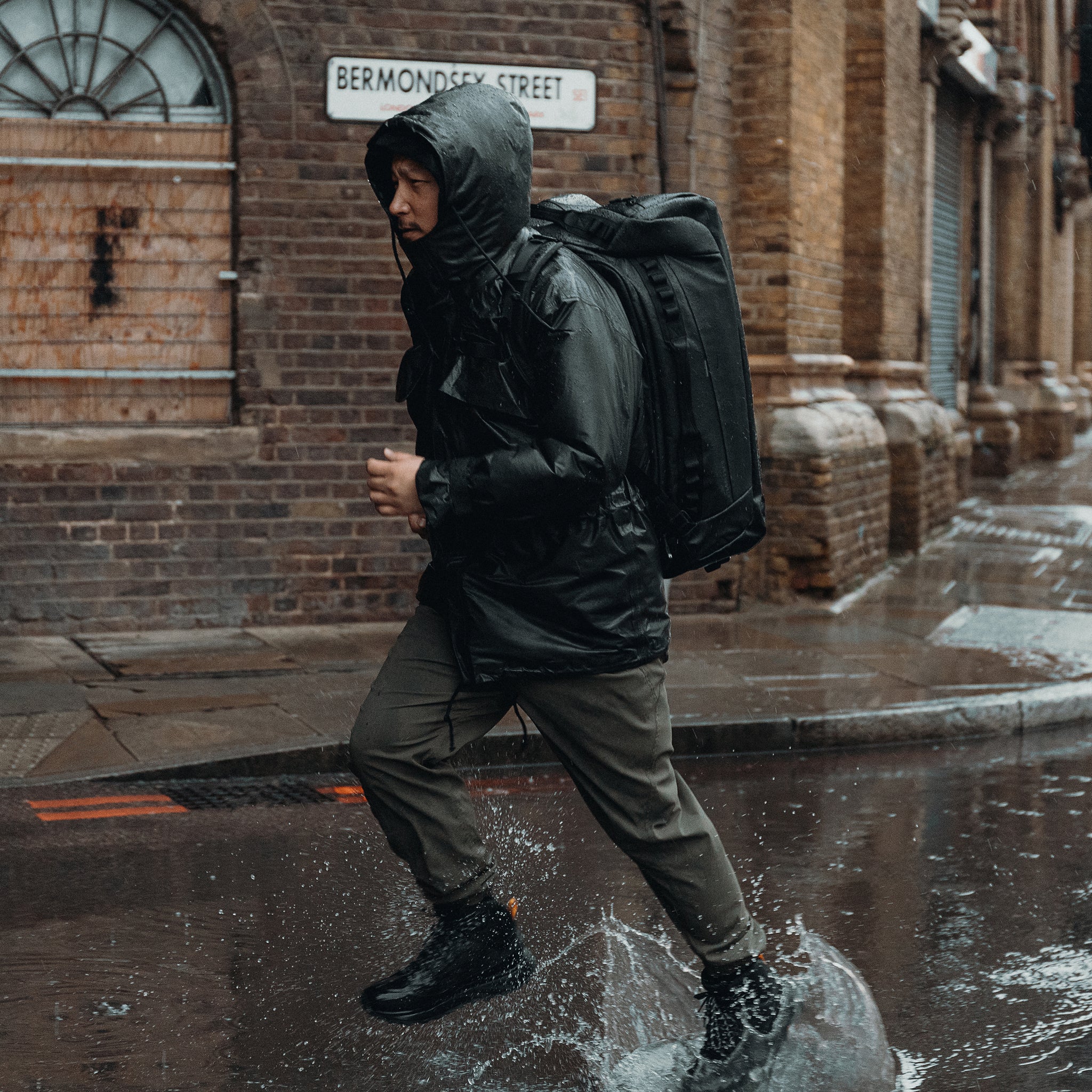 A man running through a puddle in the rain with an All Black Kit Bag 65L on his back