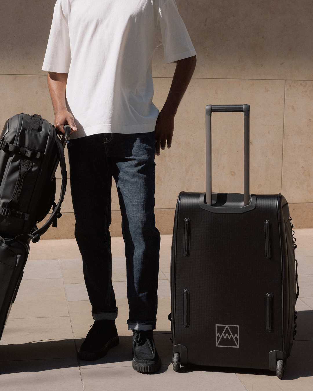 Man standing next to the Wheeled Duffel 80L in All Black. 