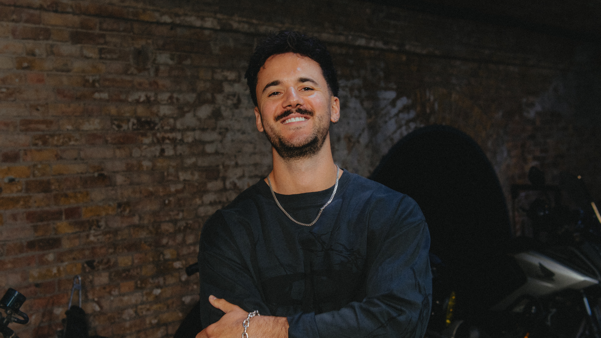 Luke Tarrant smiling at camera against brick wall background