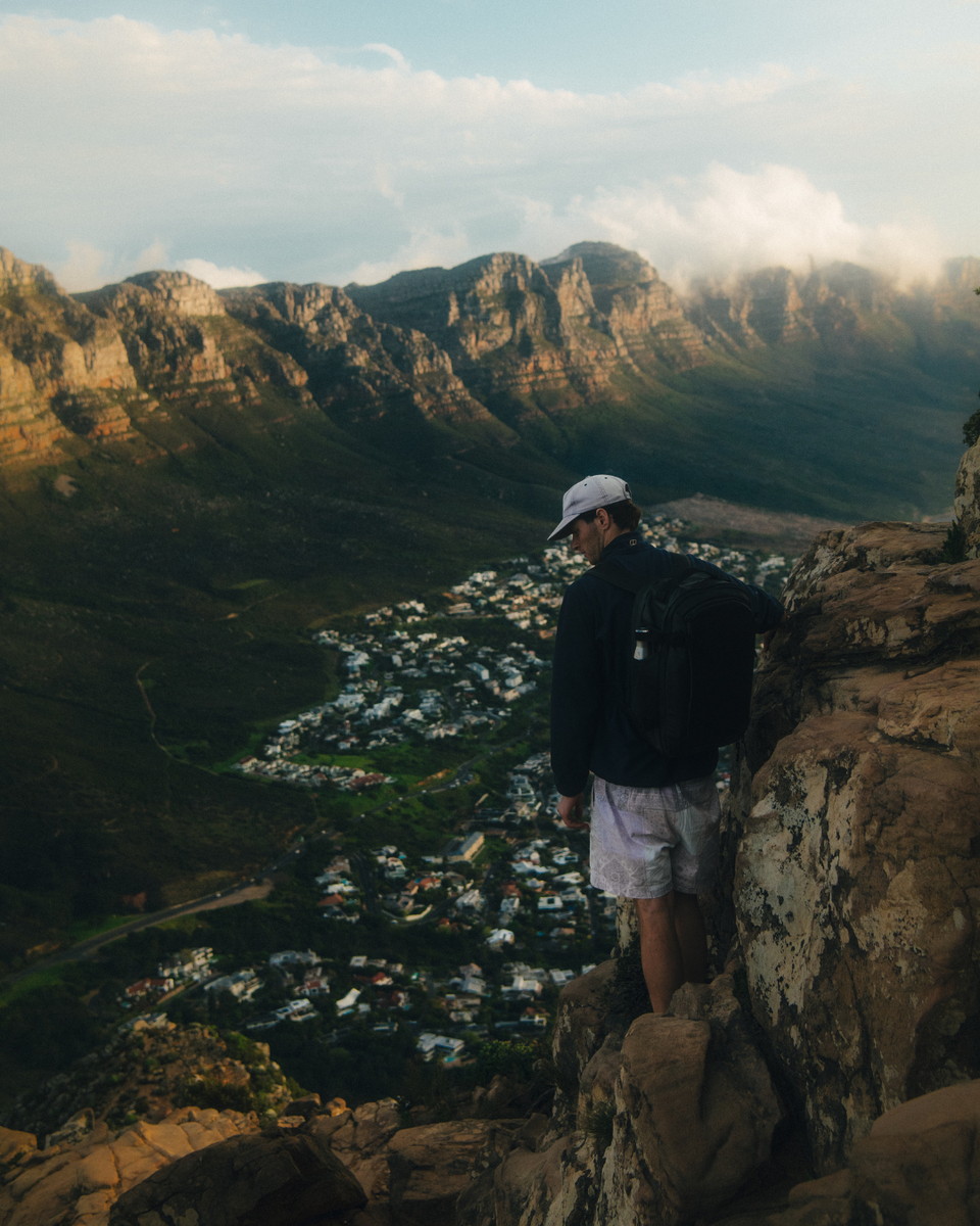 Man climbing up Lion's Head Mountain, with Cape Town city and mountain range in the background