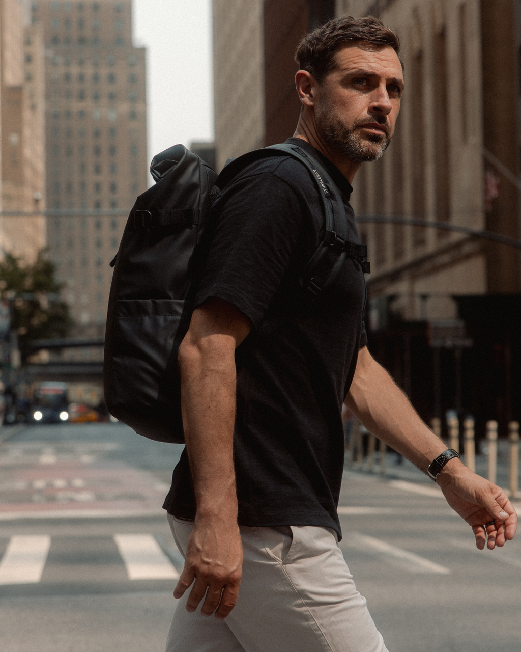Man crossing a street in New York, wearing a Roll Top Backpack in All Black.