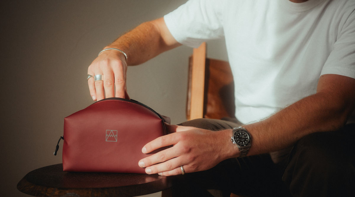 Man in a white T-shirt reaching into the Garnet Red Wash Bag.