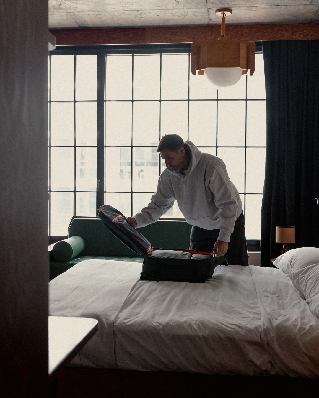 Man in a light grey jumper opening a backpack laid flat on the bed.