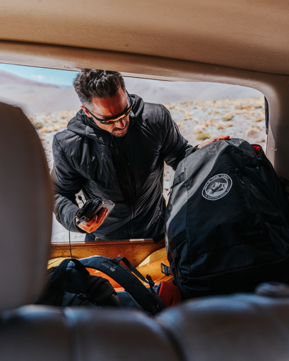 Man preparing for a journey by loading a backpack into a car with a scenic background.