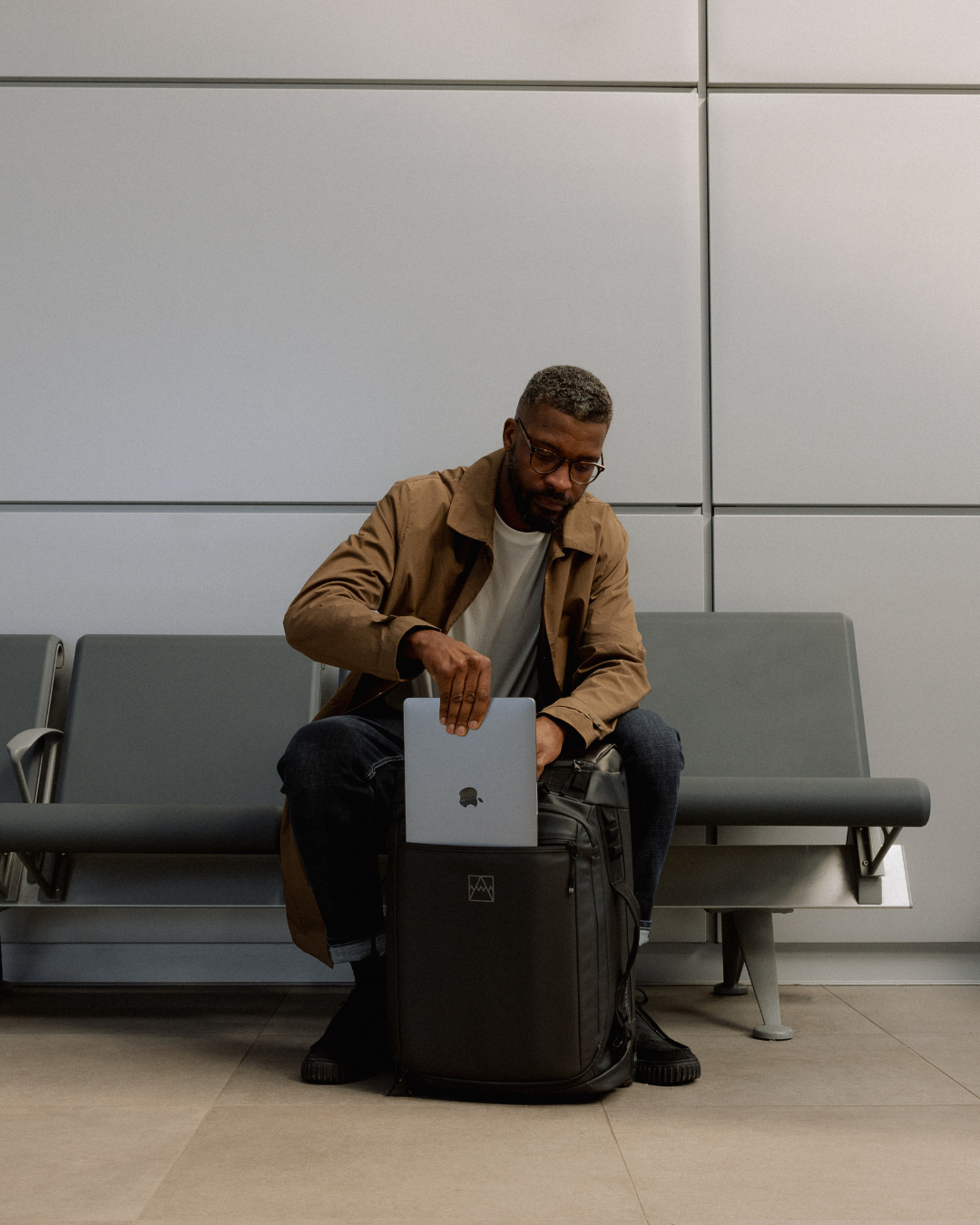 Man putting a laptop into the exterior padded laptop compartment of the All Black Wheeled Duffel 40L.
