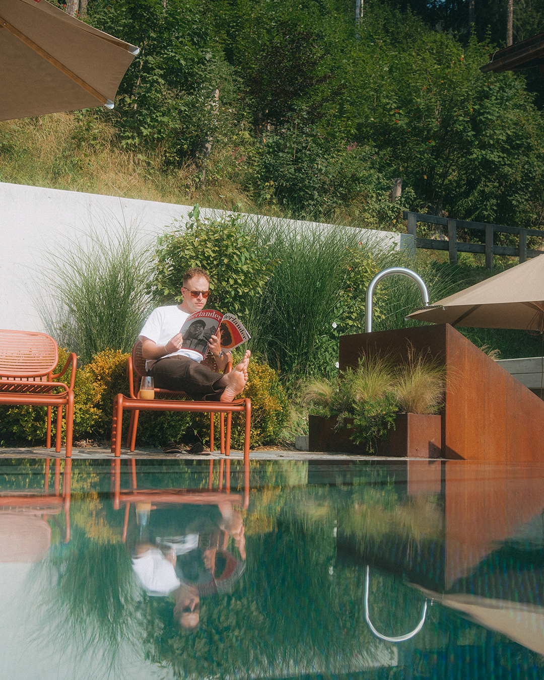Man reading a magazine by a pool with greenery in the background