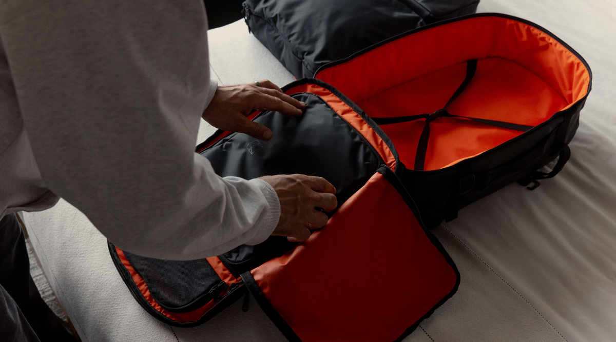 Man unpacking packing cubes from a hybrid backpack, with the orange interior visible.