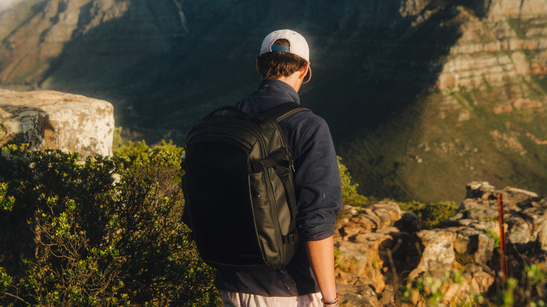 Man wearing black hybrid backpack walks up Lions Head Mountain in Cape Town