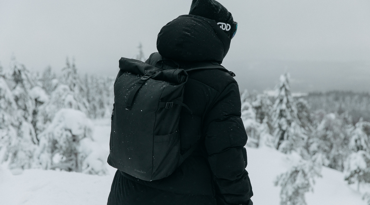 Man facing away from the camera, wearing the All Black Roll Top 20L backpack, with a snowy landscape ahead.