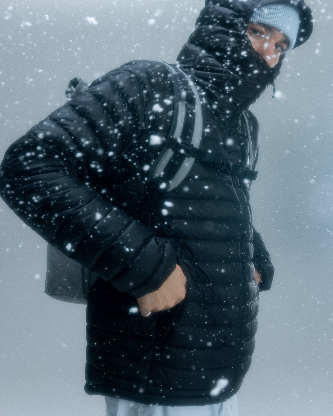 Man wearing a puffer jacket and a roll top backpack in the snow.