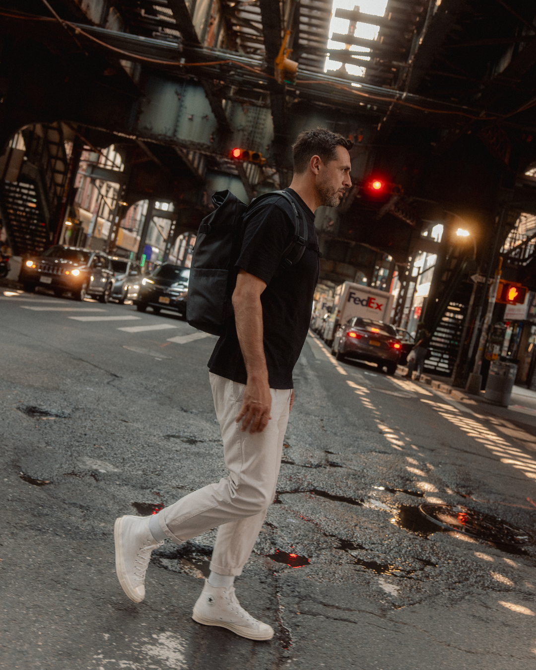 Man crossing a street in New York, wearing a Roll Top Backpack in All Black.