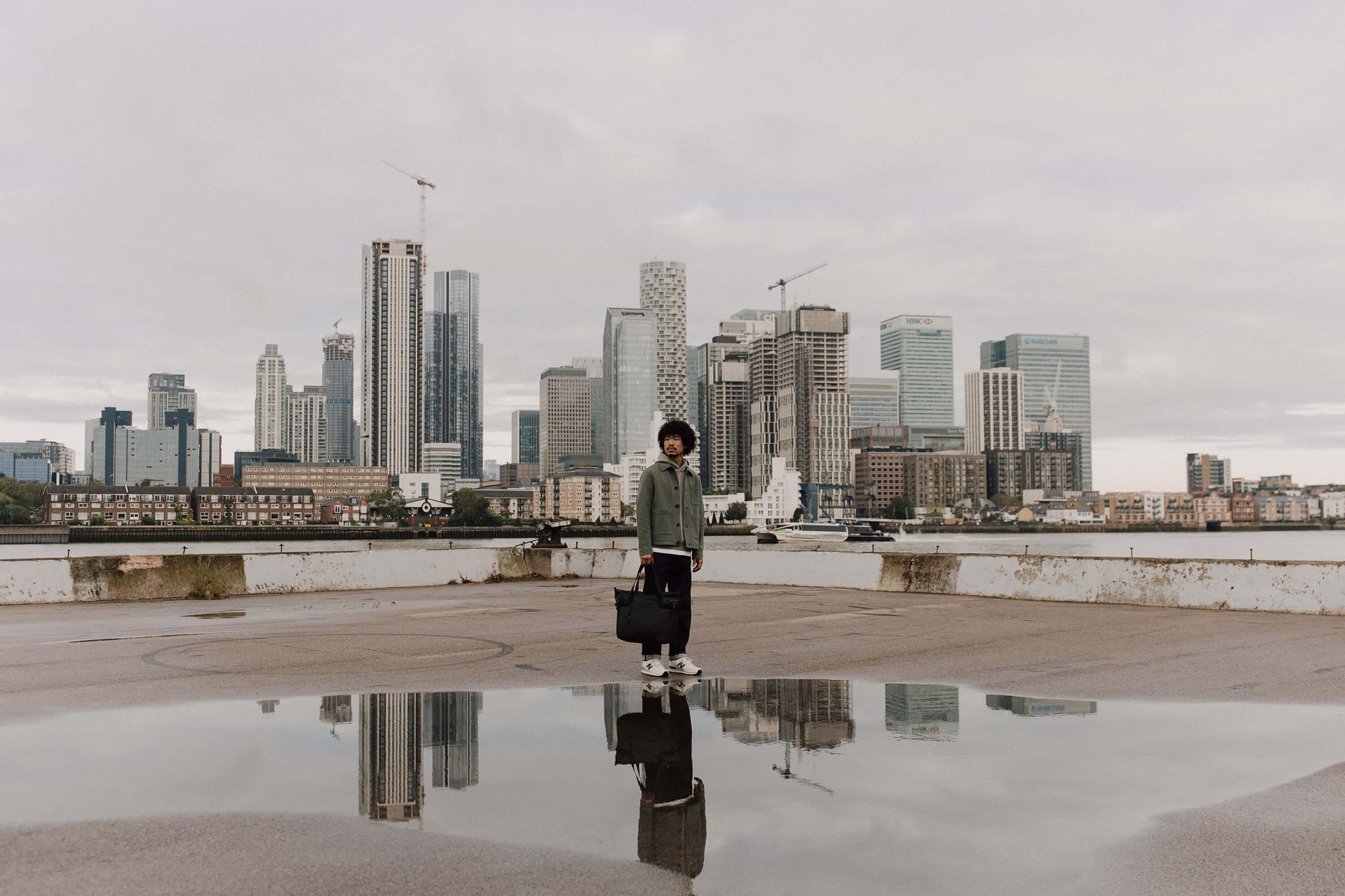 Man standing by the river with a city skyline reflection in the water